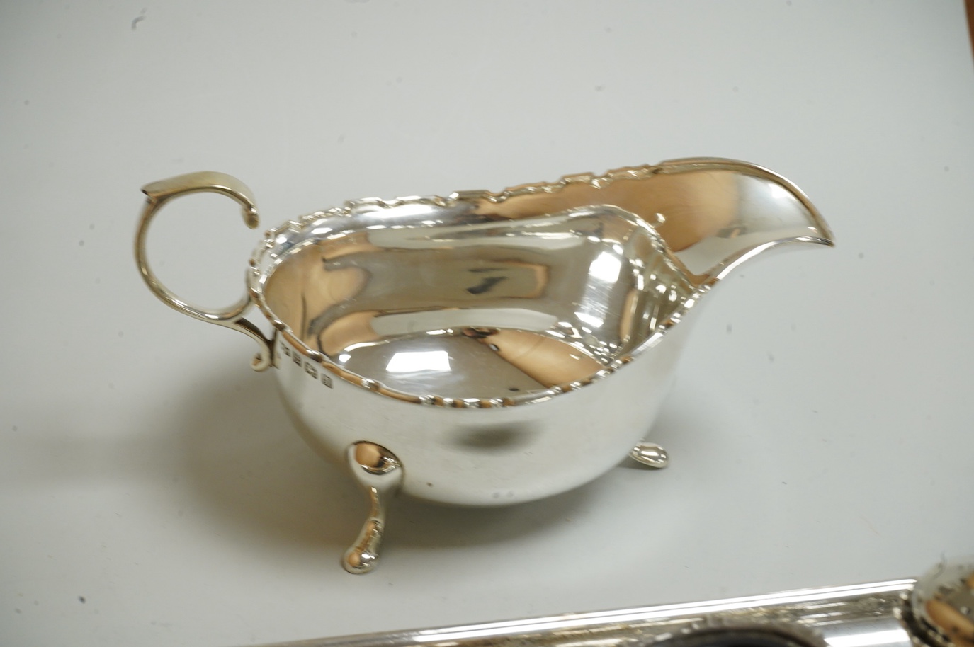 A George V silver sauceboat by Mappin & Webb, Birmingham, 1933, length 16.2cm, together with a silver salt and spoon, with blue glass liner, a silver pepperette, a pair of silver sugar tongs and a Spanish white metal two